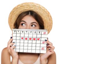 Young woman wearing a straw hat holding a menstrual calendar with heart symbols marking her period days, representing tracking cycles and menstrual treatment in Bhopal.